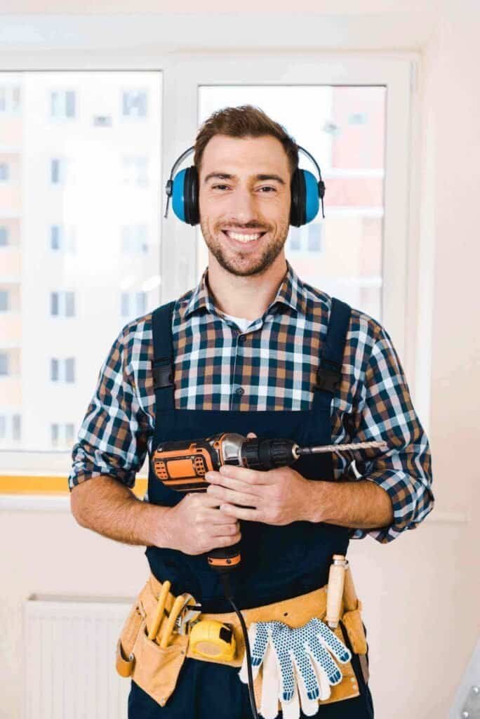Professional drain cleaning technician smiling while holding a power drill during a plumbing service in Dallas, TX.